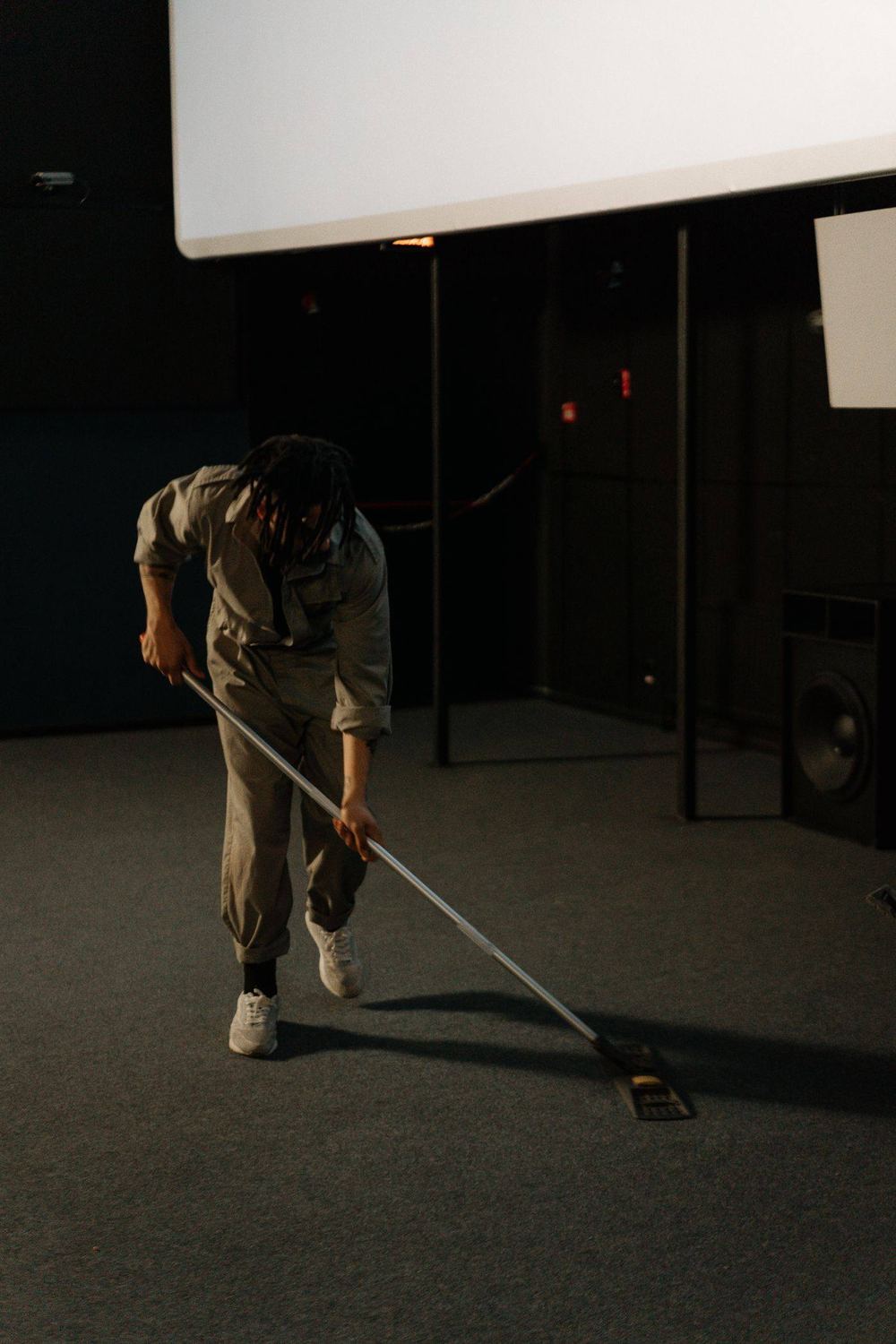 A person in a gray work uniform sweeping a commercial carpet.