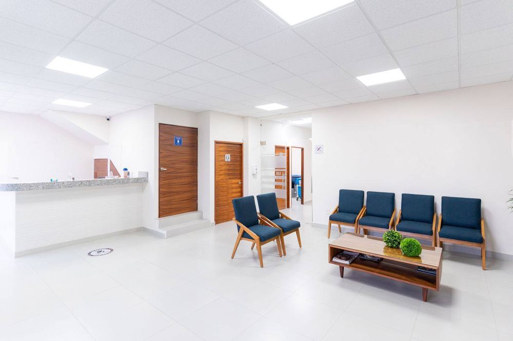 Clinic waiting room with chairs, a reception desk, and exam-room doors.