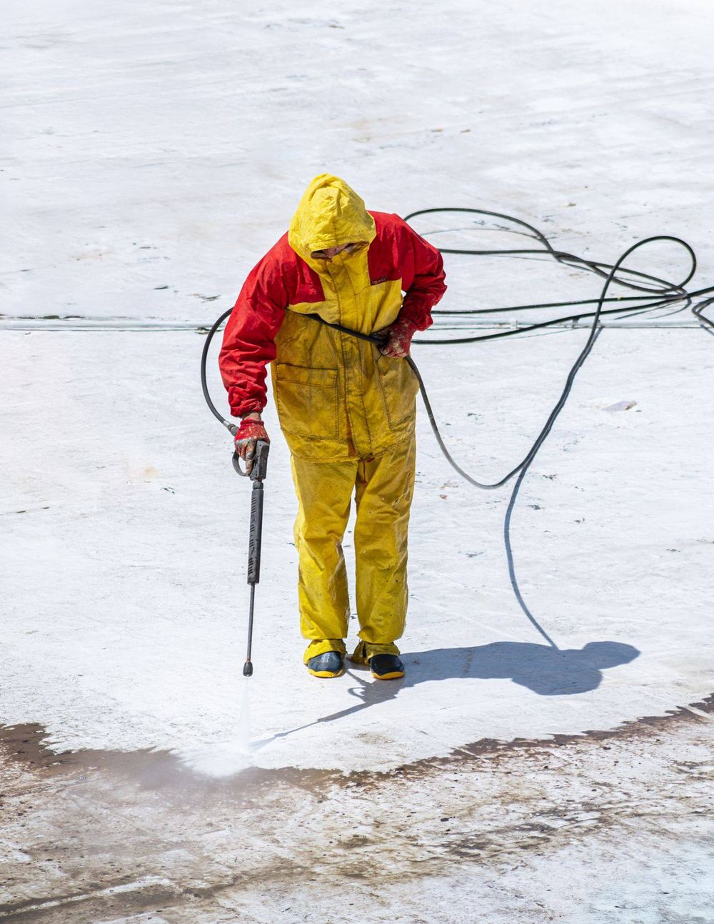A worker in a yellow rain suit pressure-washing a flat exterior surface.